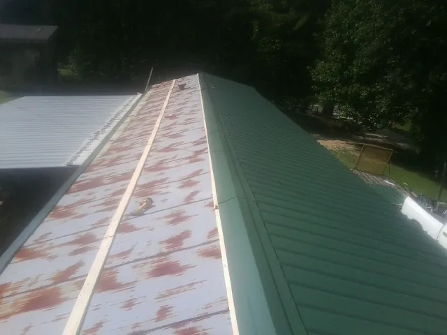 Old rusted panels beside newly installed green metal roofing — Wind Damage Roof Repair by Roofing Brothers in Tupper Lake