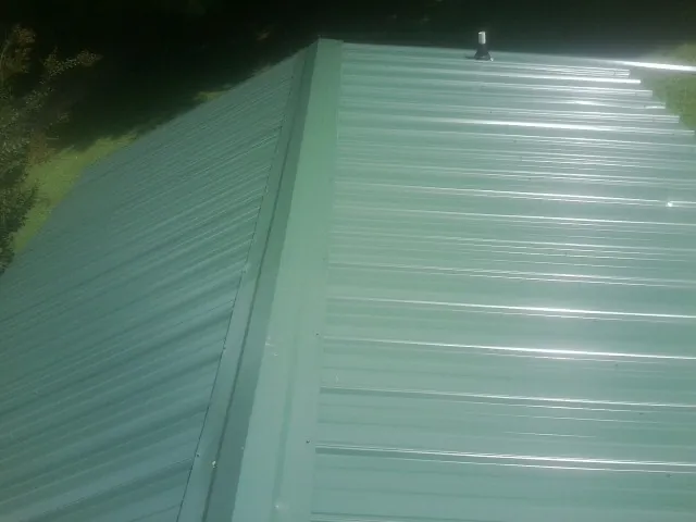 New green metal panels meeting at the ridge of a roof — Flat Roof Repair work by our crew in Tupper Lake