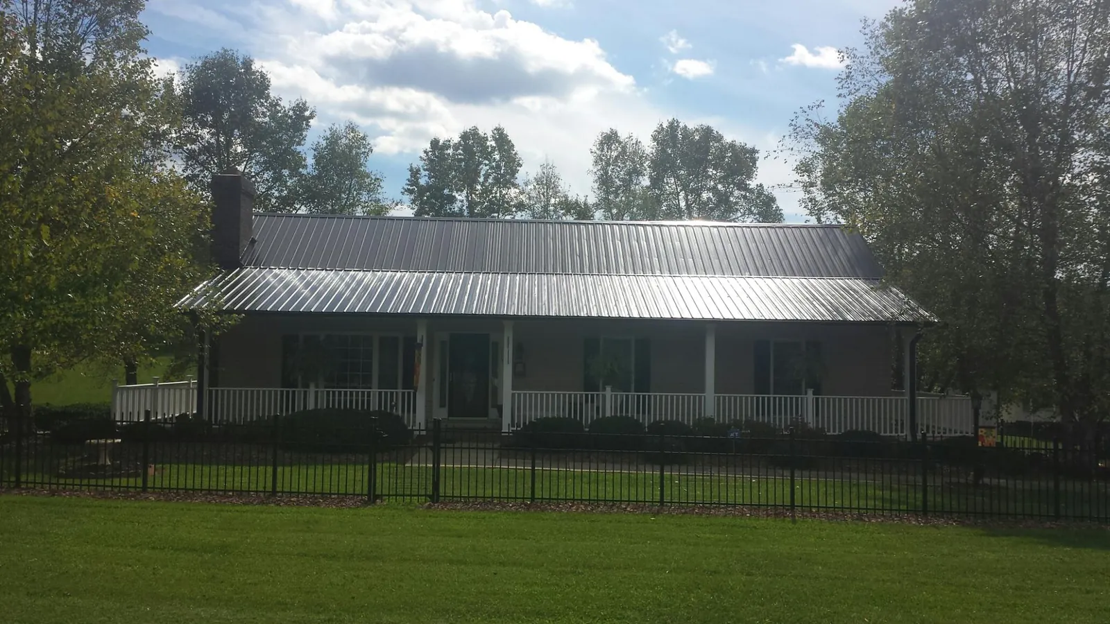 Gray metal roof on a brick ranch with a full width front porch — Gutter Guard Installation work by our crew in Tupper Lake