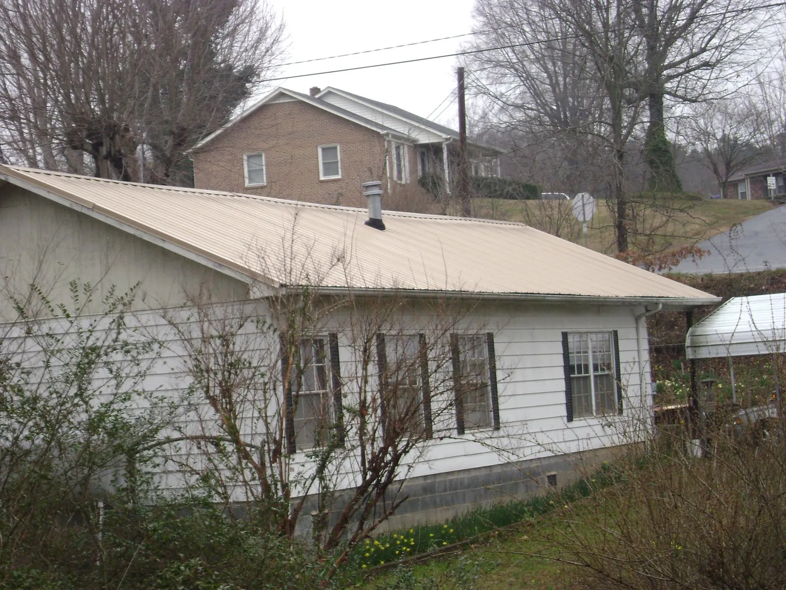 Tan metal roof on a white sided house set into a hillside — Commercial Roofing by Roofing Brothers in Tupper Lake