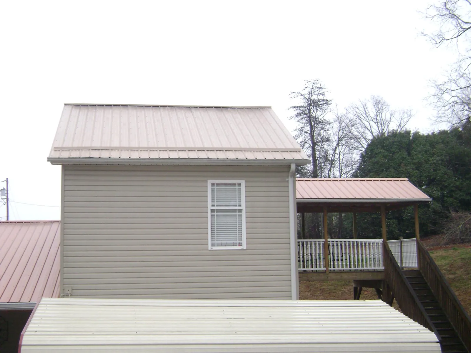 Tan metal roofs on a two story addition and attached porch, from a Roof Replacement job in Tupper Lake