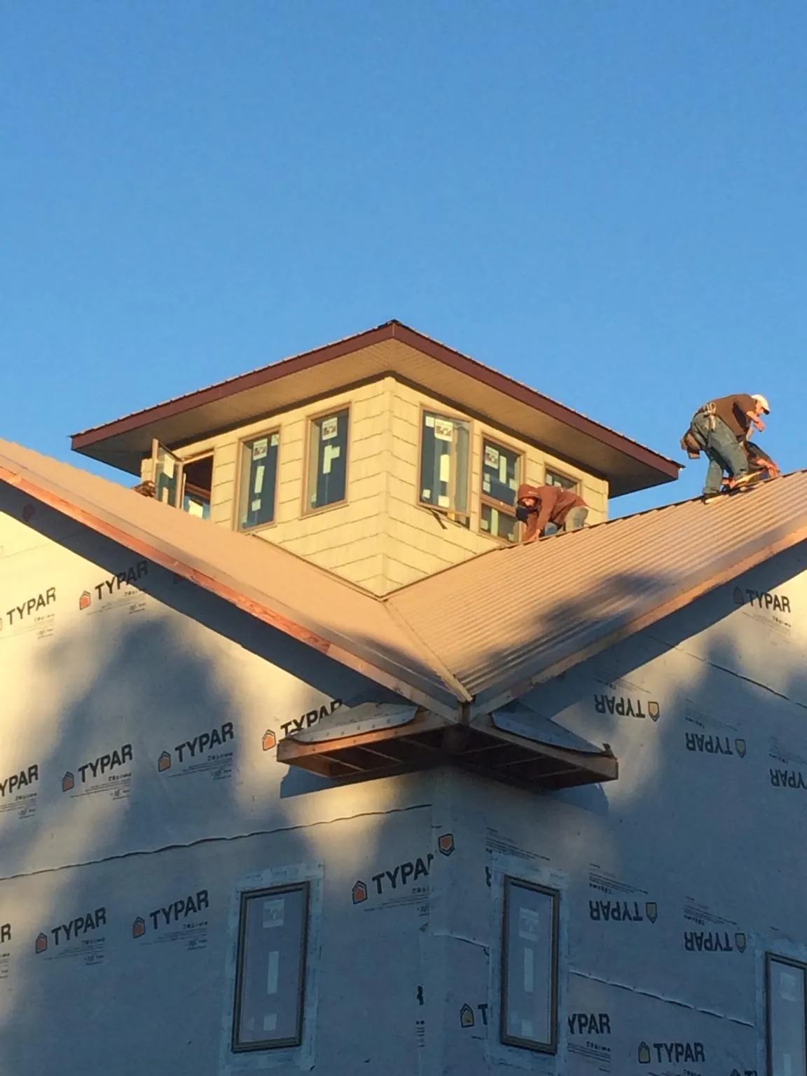 Roofers working around a rooftop cupola on a new metal roof at sunset — Roof Waterproofing in Tupper Lake by Roofing Brothers